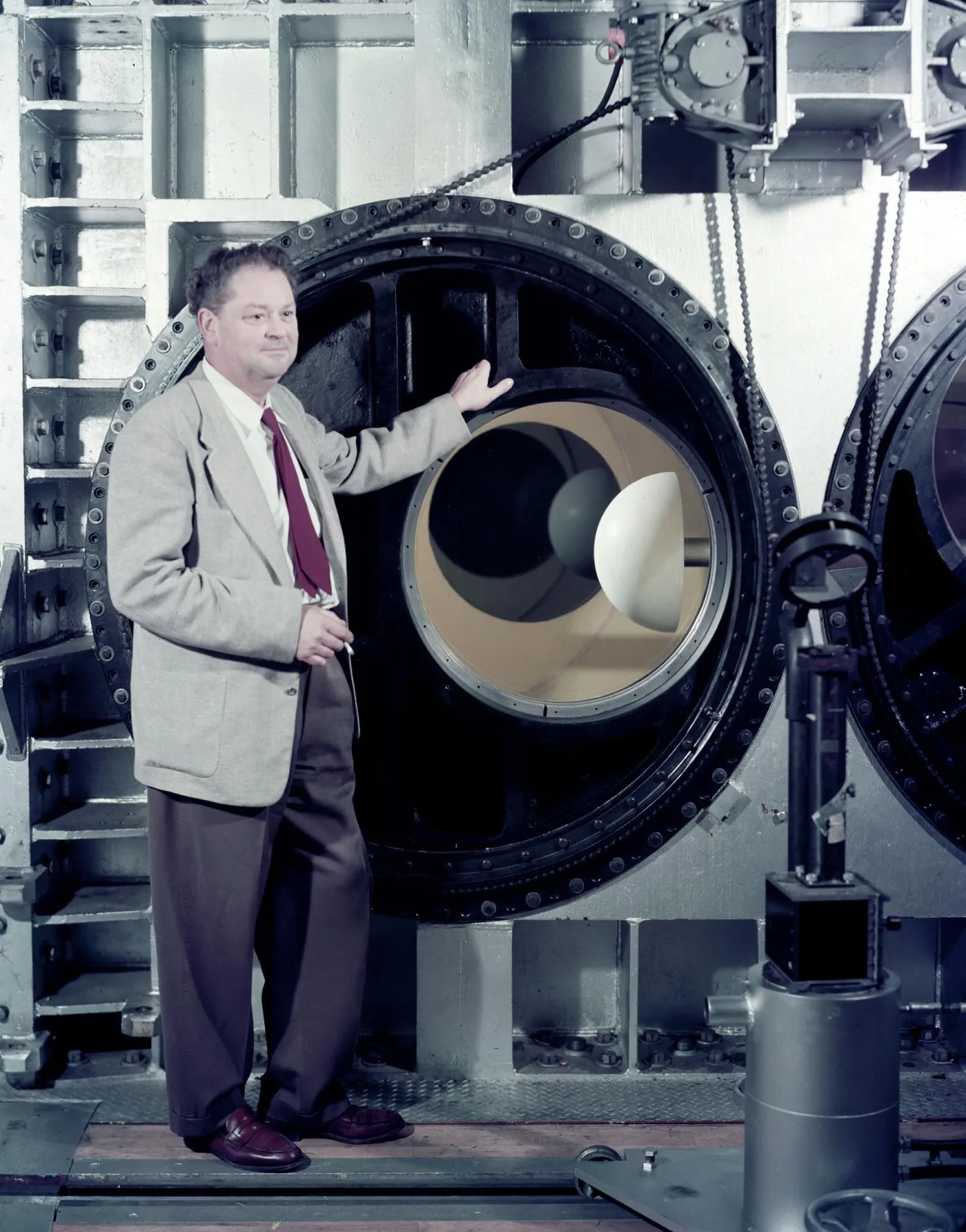 H. Julian Allen standing beside the round test-section window of a large wind tunnel, with a hemispherical blunt-body model mounted inside