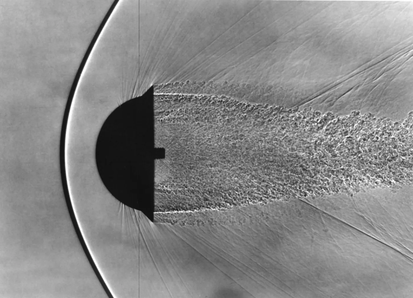 Shadowgraph of a hemispherical model in free flight with a curved bow shock standing well ahead of its rounded face and a turbulent wake behind