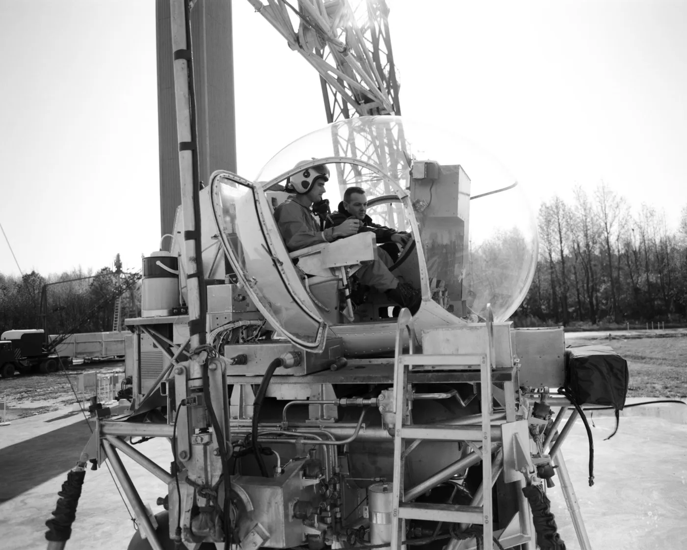Astronaut Roger Chaffee beside an open-frame lunar landing test vehicle under the gantry at Langley