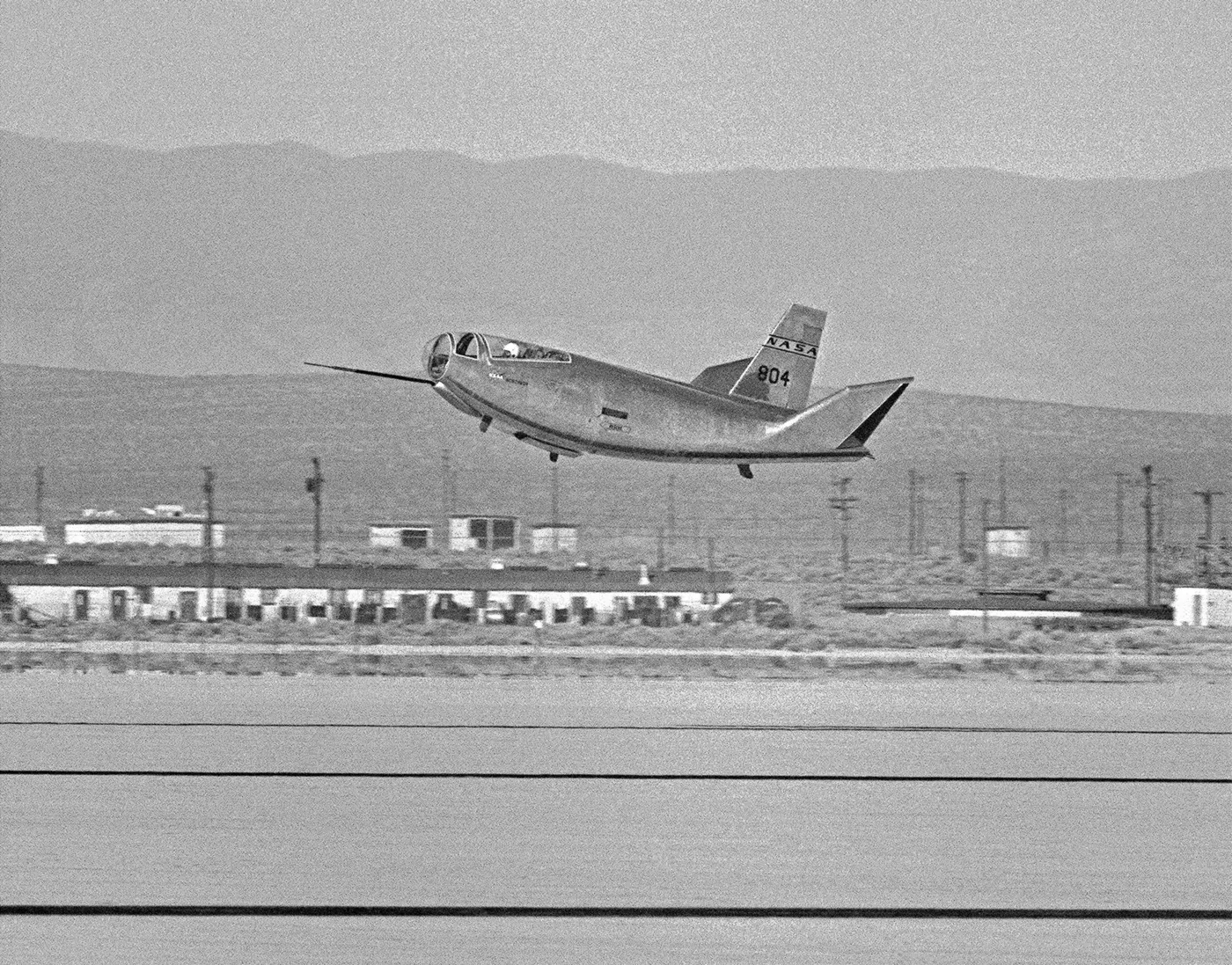 The HL-10 lifting body just above a dry lakebed, nose high, moments before touchdown