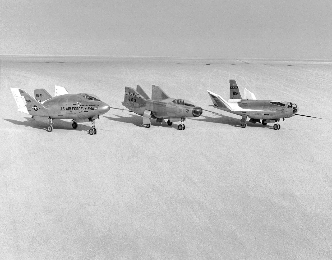 Three wingless lifting-body aircraft parked side by side on a flat dry lakebed